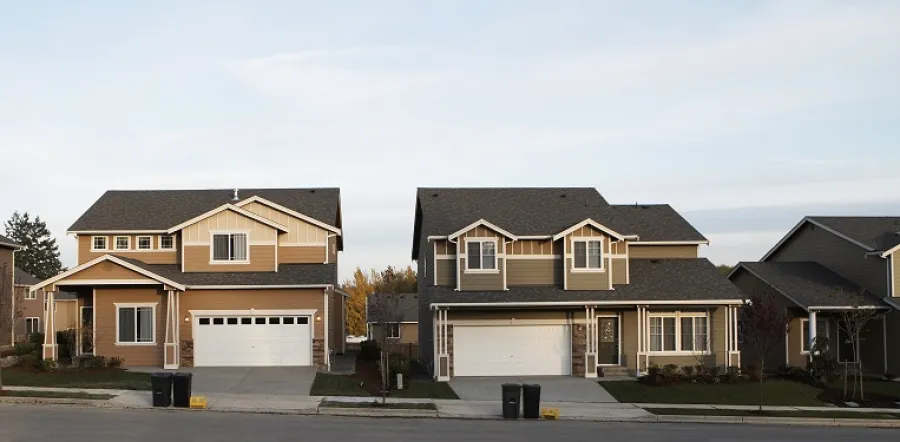 Two modern suburban houses with garages and driveways under a clear sky in a residential neighborhood.