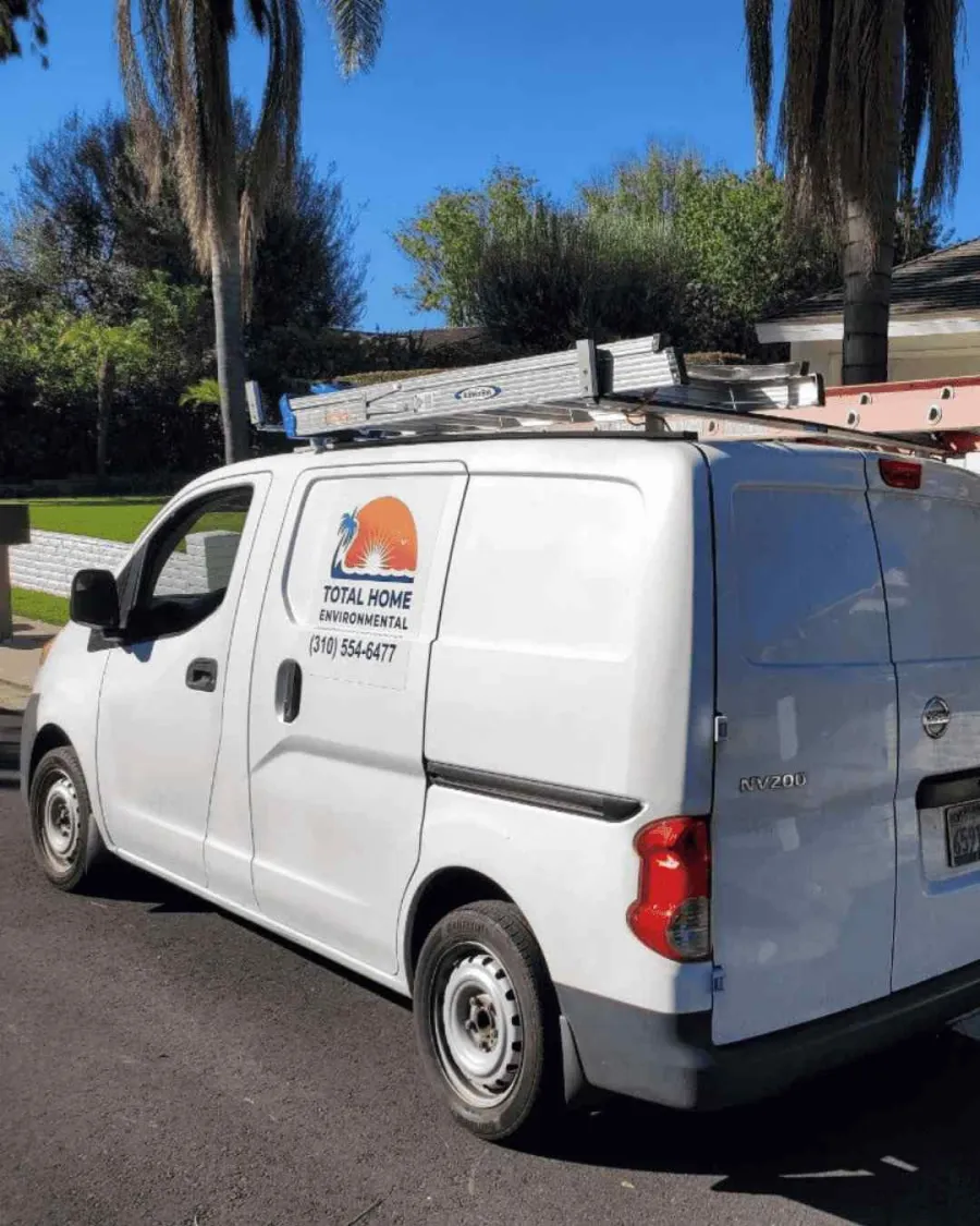 White Total Home Environmental service van with ladders on roof parked on residential street under palm trees