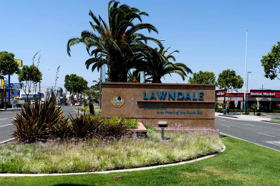 Lawndale city entrance sign with palm trees, greenery, and blue sky on a sunny day near urban street.