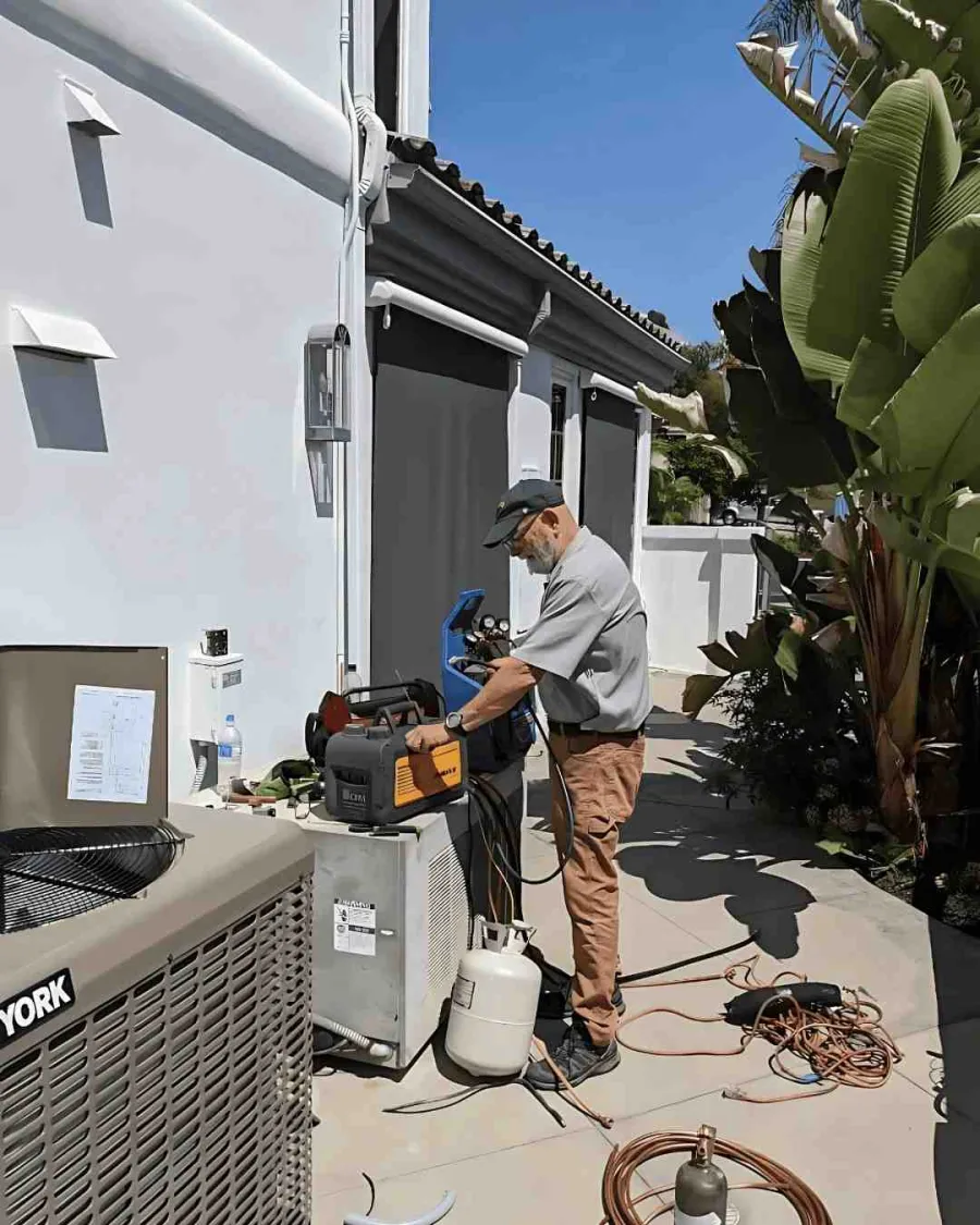 torrance ca Technician servicing air conditioning units outside a white building on a sunny day with tropical plants nearby