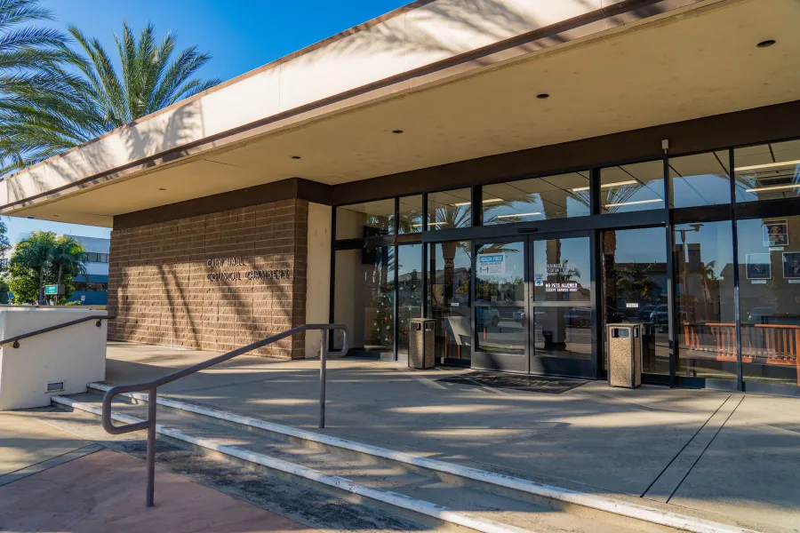 City Hall and council chambers building with glass doors, palm trees, and concrete steps in sunny weather.