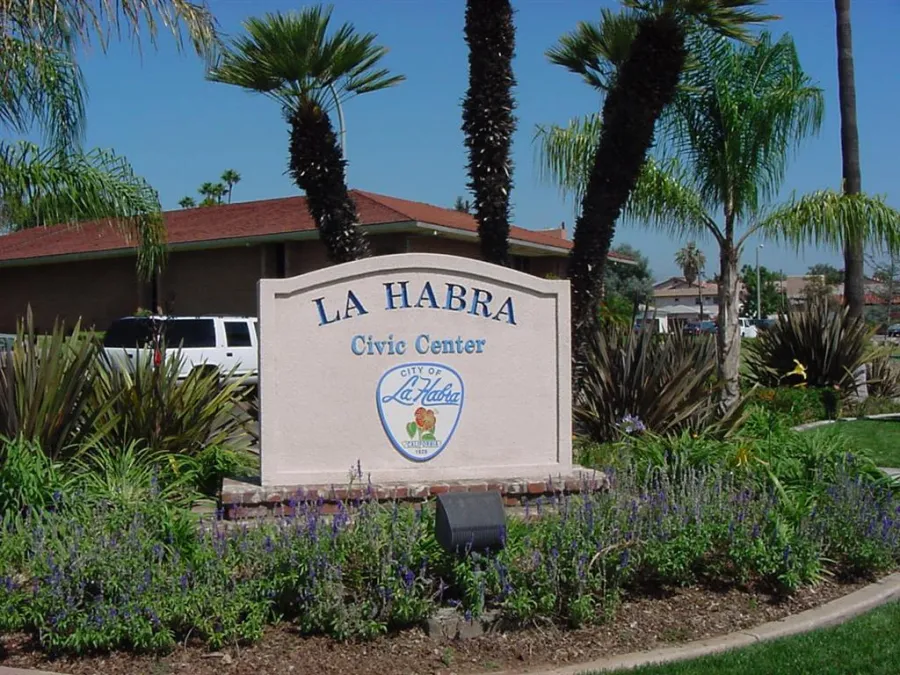 La Habra Civic Center sign surrounded by palm trees and landscaped plants under a clear blue sky.