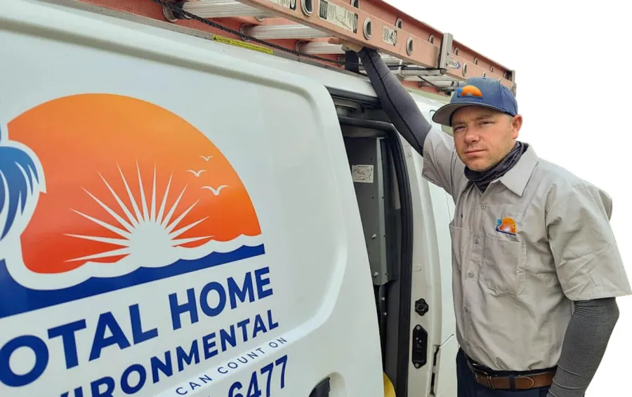 Technician leaning on a Total Home Environmental service van with company logo and ladder on top