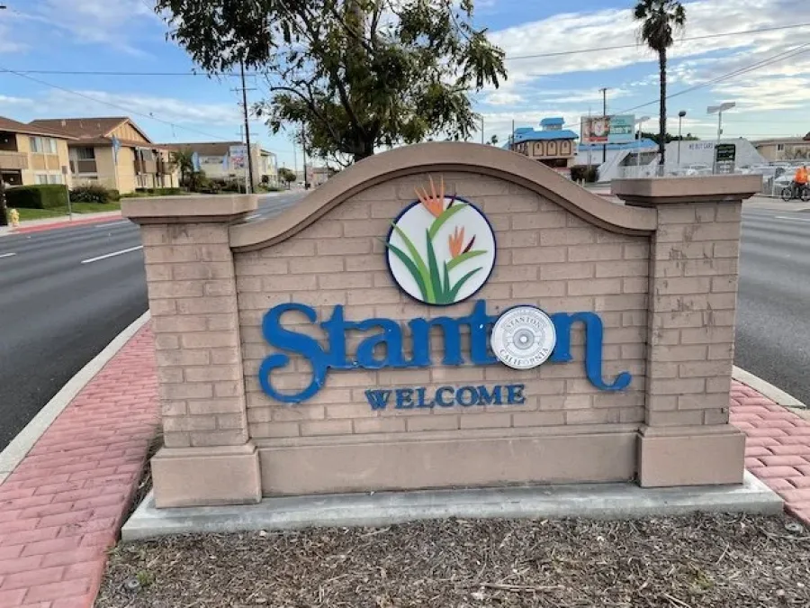 Welcome sign for Stanton, California featuring blue text and a bird of paradise flower emblem on a brick base.