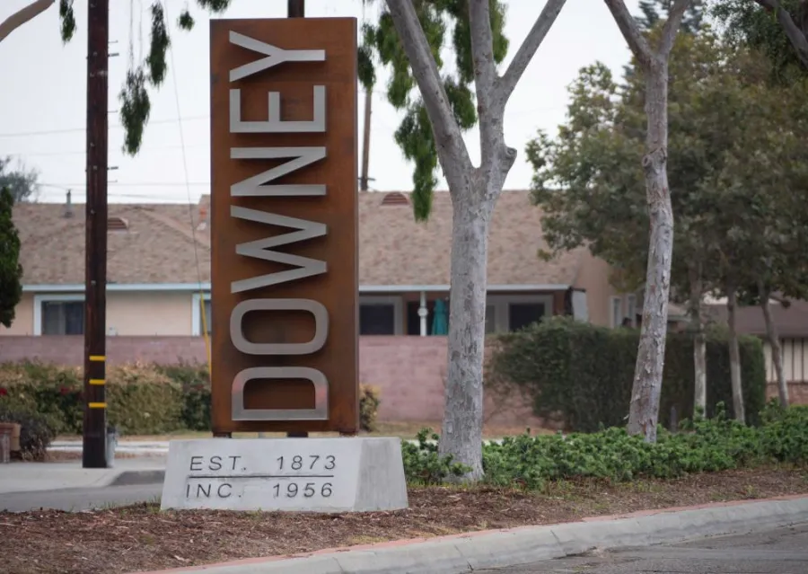 Large vertical Downey city sign with establishment dates set in a suburban tree-lined street area