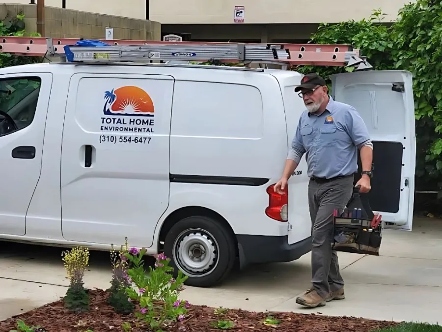 Los Angeles Technician walking with toolbox near white Total Home Environmental service van with ladder on roof in driveway.