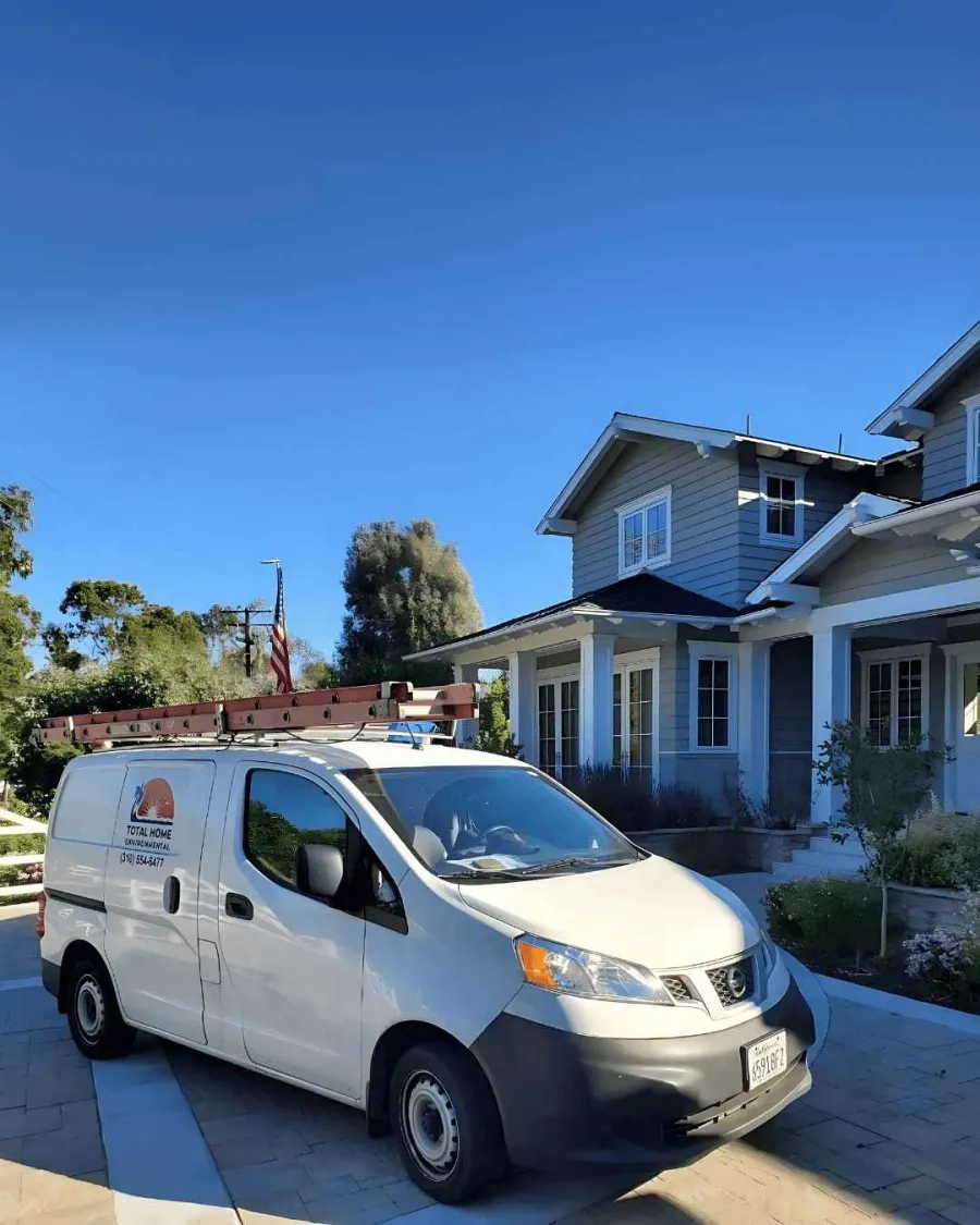 White service van with ladder parked outside a suburban gray house on a sunny day