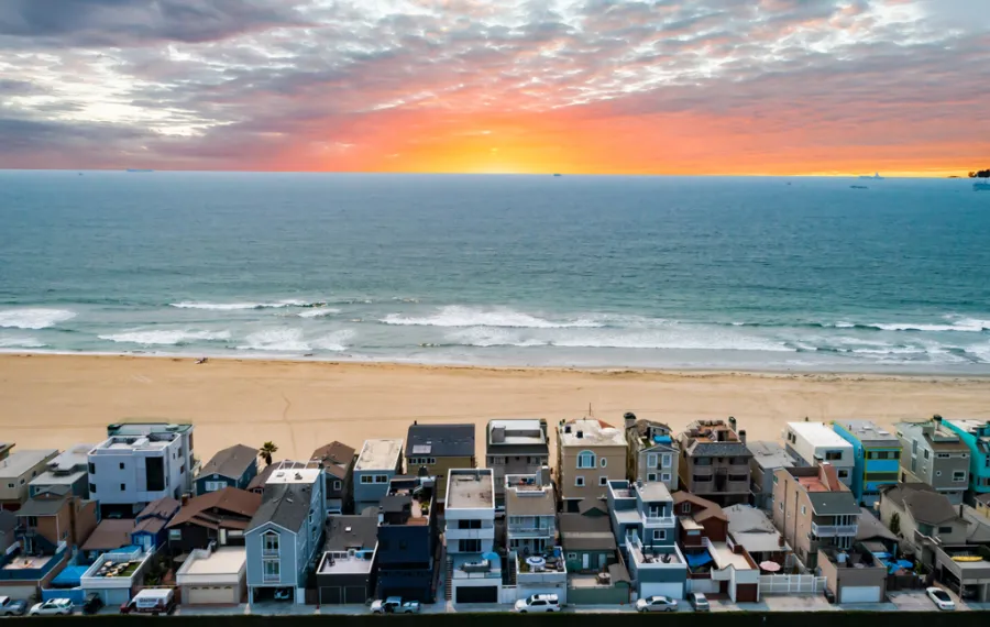 Sunset over ocean waves with a sandy beach in Surfside, CA and densely packed beachfront houses in foreground.