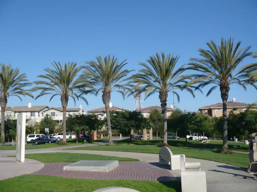 Palm trees in Signal Hill line a sunny park with benches, walking paths, and residential buildings under a clear blue sky.
