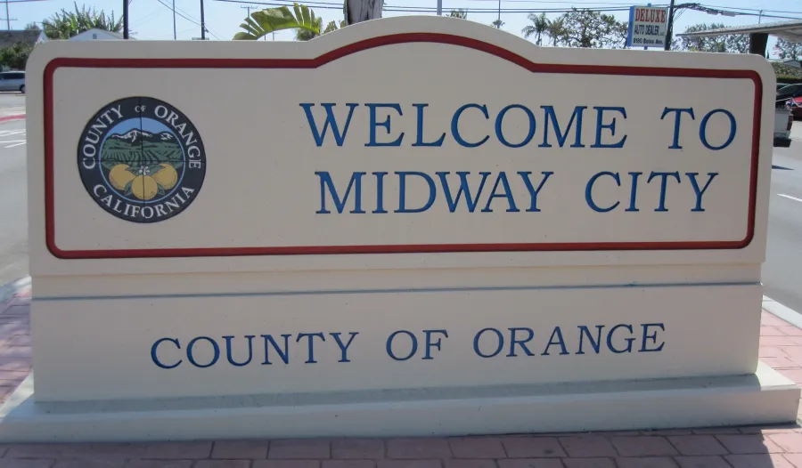 Welcome sign for Midway City in County of Orange with county seal and street background