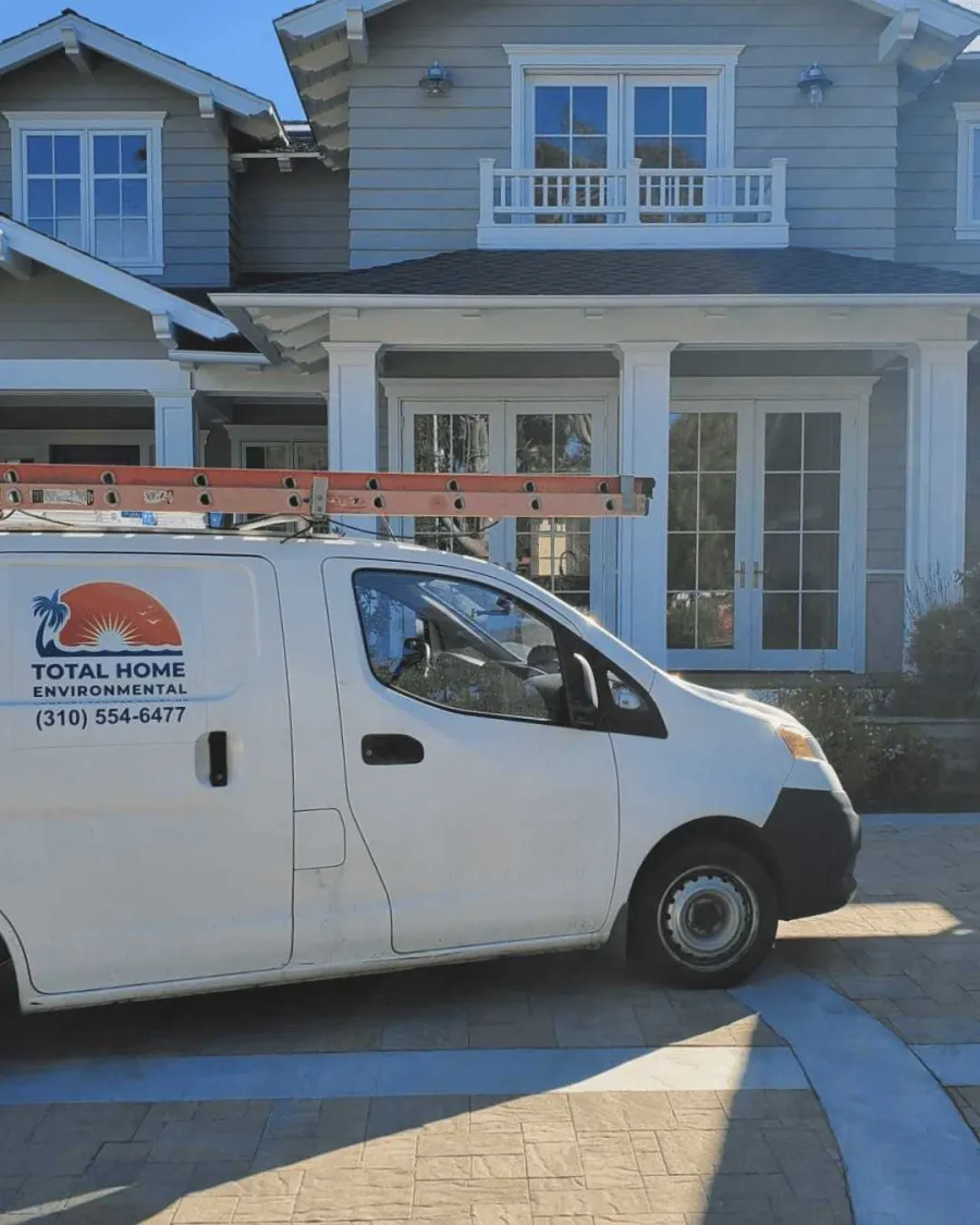 White service van with ladder parked outside a modern two-story gray house on a sunny day.