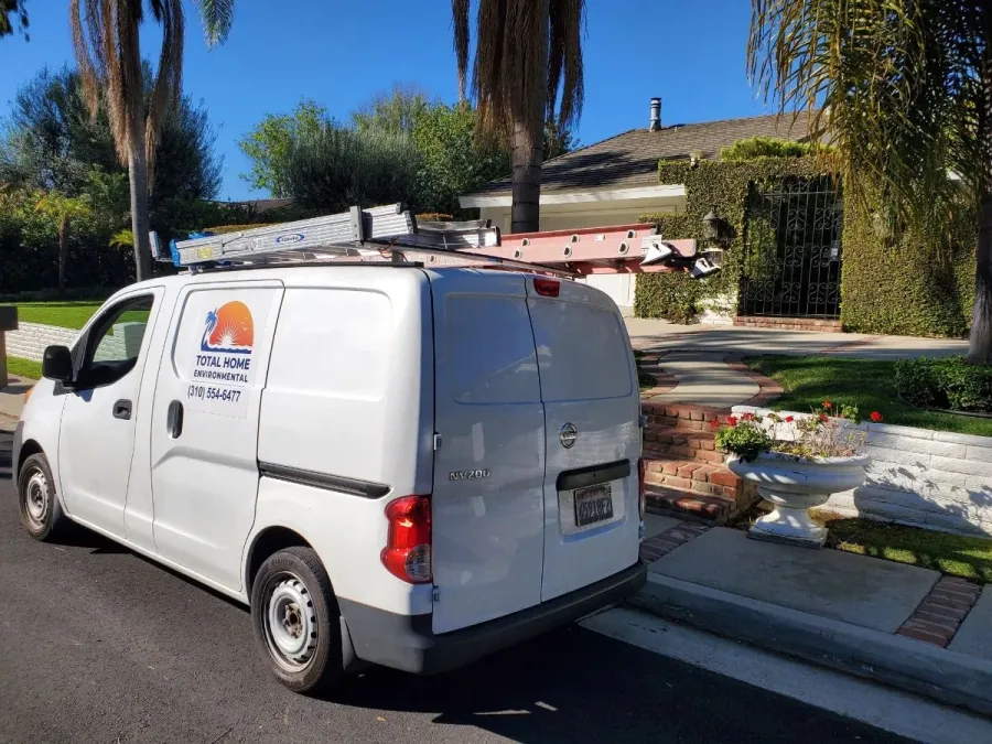 White service van with ladders on roof parked in front of residential home on sunny day