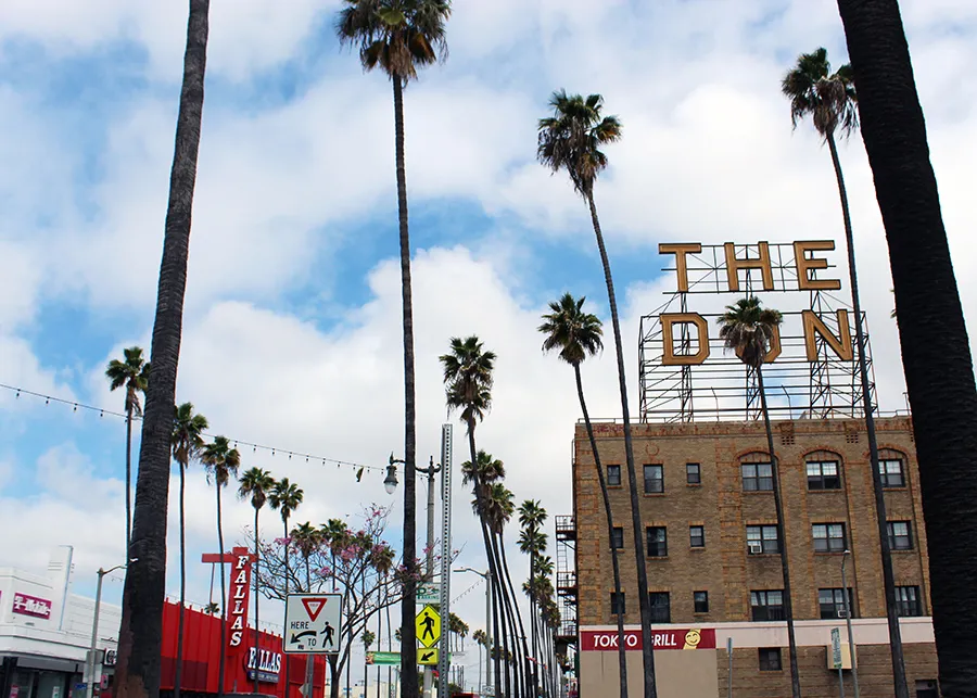Tall palm trees line a street with The Don sign in Wilmington, CA atop a brick building under a blue sky with clouds.