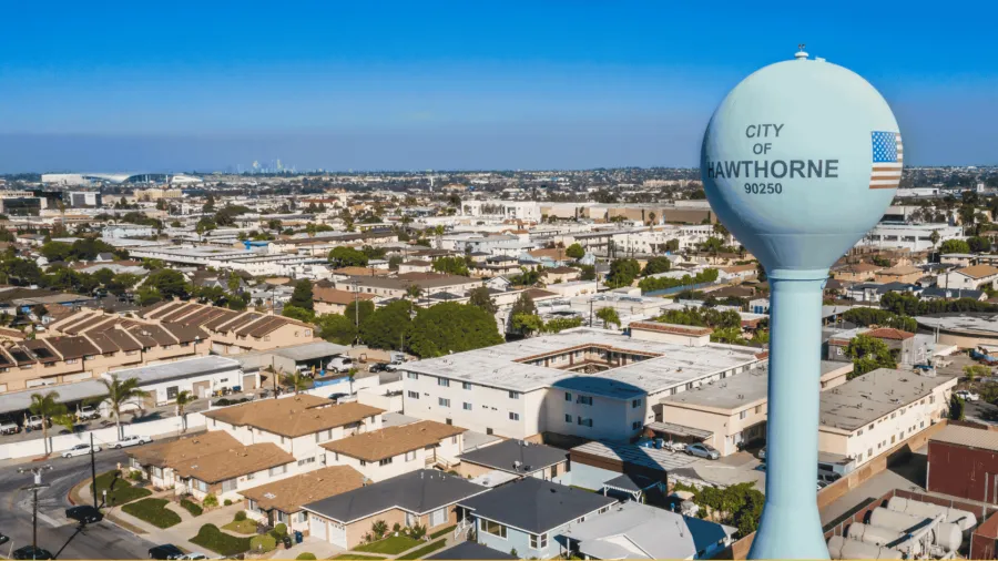 Aerial view of Hawthorne city with residential houses and a water tower marked City of Hawthorne 90250 under clear blue sky.