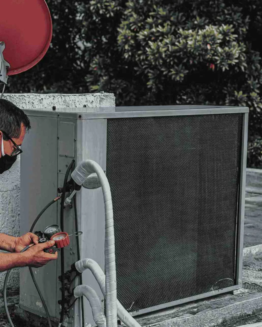 Technician wearing a mask inspecting and measuring an outdoor air conditioning unit with gauges and hoses.