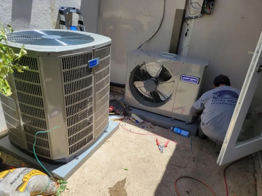 Technician installing or repairing two air conditioning units outside a house on a sunny day