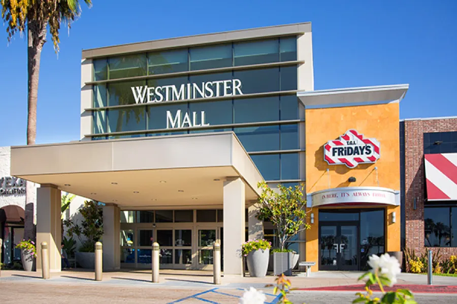 Entrance of Westminster Mall with TGI Fridays restaurant under a clear blue sky and palm trees.