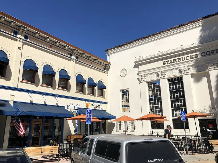 Historic Starbucks coffee shop with outdoor seating under clear blue sky and adjacent building with blue awnings.