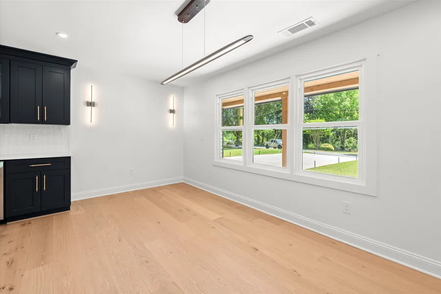 Bright modern room with light wood flooring, black cabinets, white walls, and large windows with outdoor view