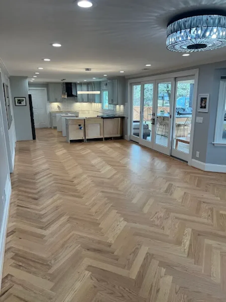 Bright open kitchen and living area with chevron hardwood floors and large glass doors leading outside.