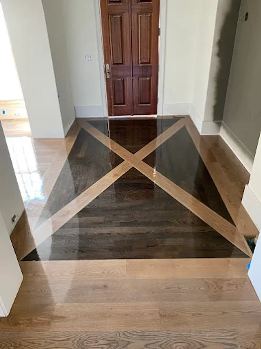 Polished hardwood floor with a geometric X pattern in front of wooden double doors in a hallway.