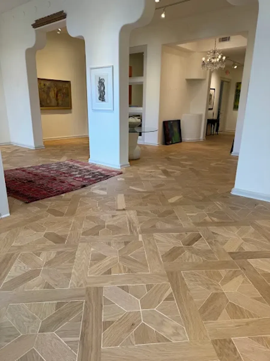 Intricate wooden parquet flooring in a bright art gallery with white walls and framed artwork.