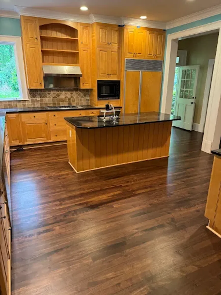 Spacious kitchen with wooden cabinets, dark granite countertops, a central island, and hardwood flooring.