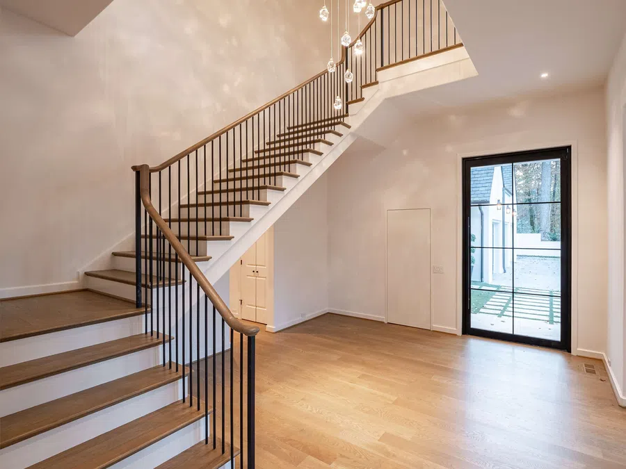 Modern interior with wooden staircase, black metal railing, hardwood floor, and glass door leading outside.