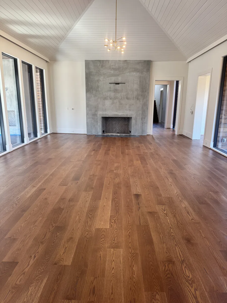 Spacious room with polished wood floors, concrete fireplace, white vaulted ceiling, and large glass doors.
