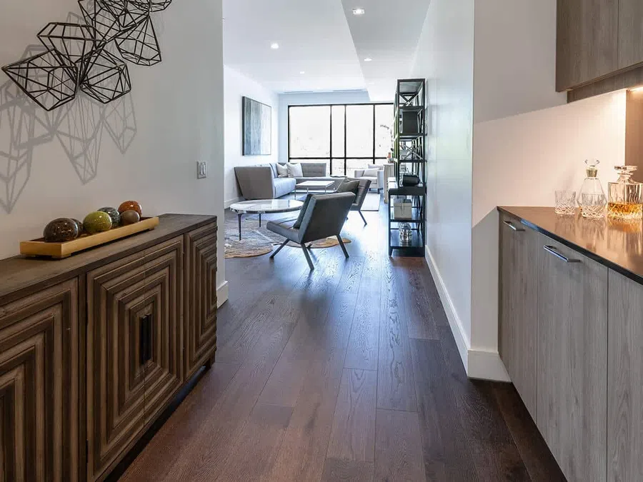 Modern living room with dark hardwood floors, gray chairs, wooden cabinets, and geometric wall art.