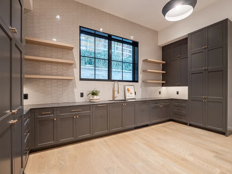 Modern kitchen with gray cabinets, light wood flooring, open shelves, and a large window with natural light.