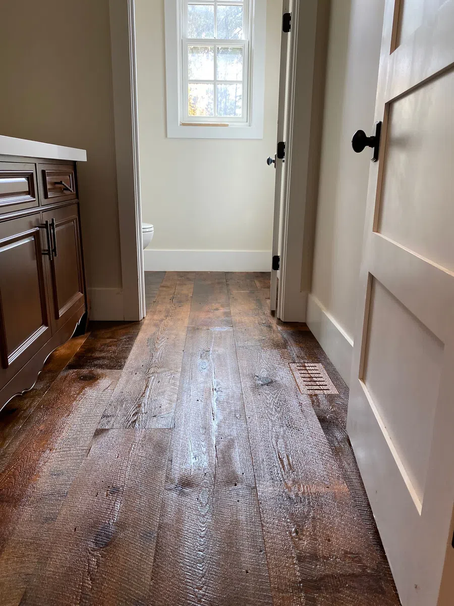 Rustic hardwood floor leading to light-filled room with white walls and brown cabinetry on the side.
