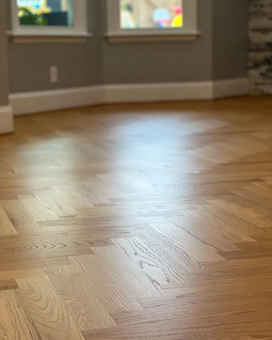 Close-up of smooth, polished hardwood floor with herringbone pattern in a bright room.