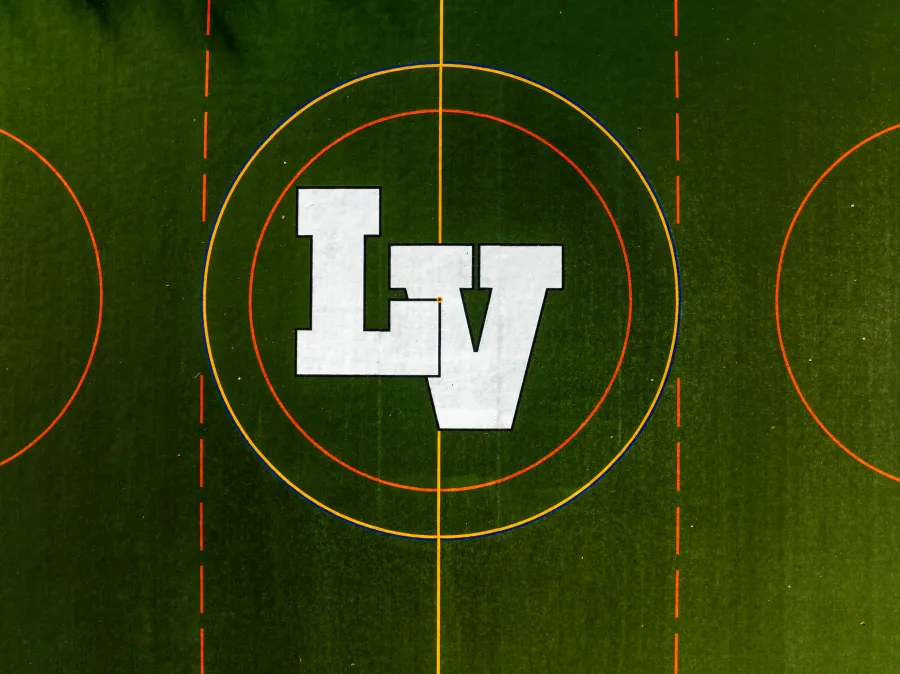 Aerial view of a sports field with green turf and white letters LV in the center circle surrounded by colored lines.
