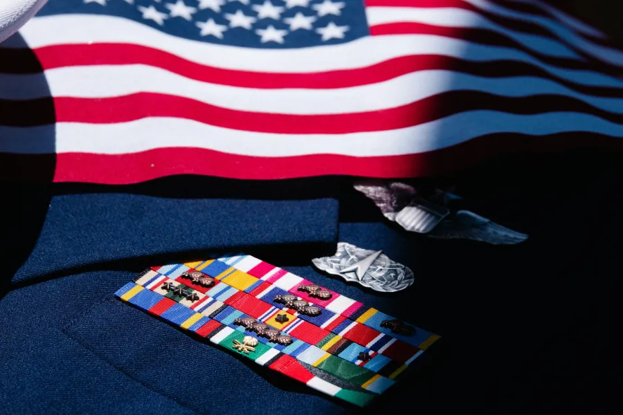 Close-up of military ribbons and medals on a uniform beneath a partially visible American flag.