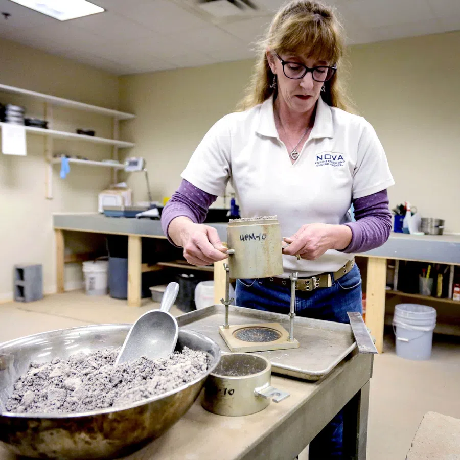 Woman in lab coat handling soil samples with sieves and metal scoop in a lab testing environment
