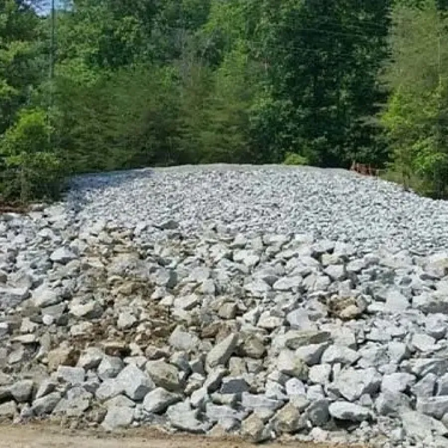 Large pile of gray rocks surrounded by green trees in a forested area under daylight.