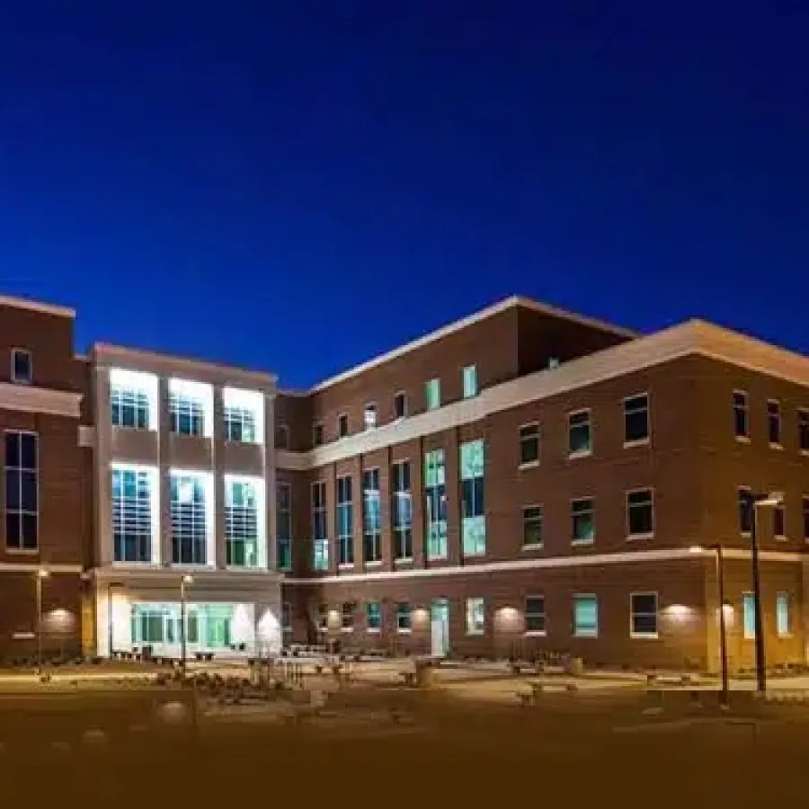 Modern brick building with large windows illuminated at dusk under a deep blue sky