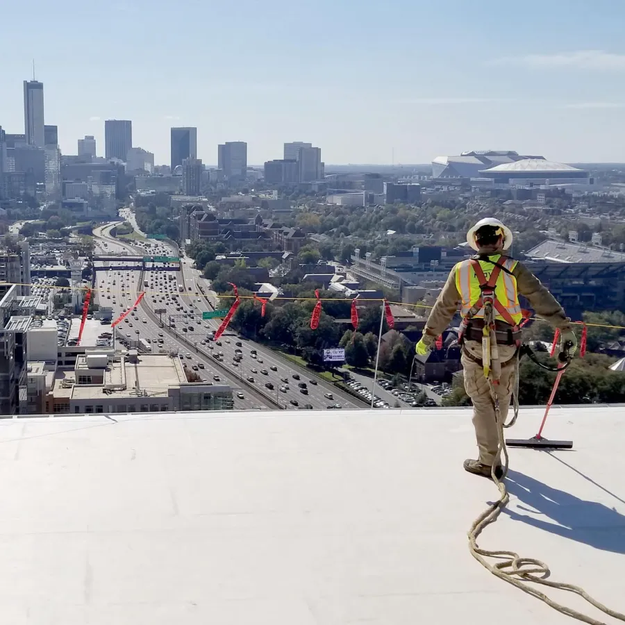 Construction worker in safety gear overlooking city skyline and busy highway from a high rooftop on a sunny day