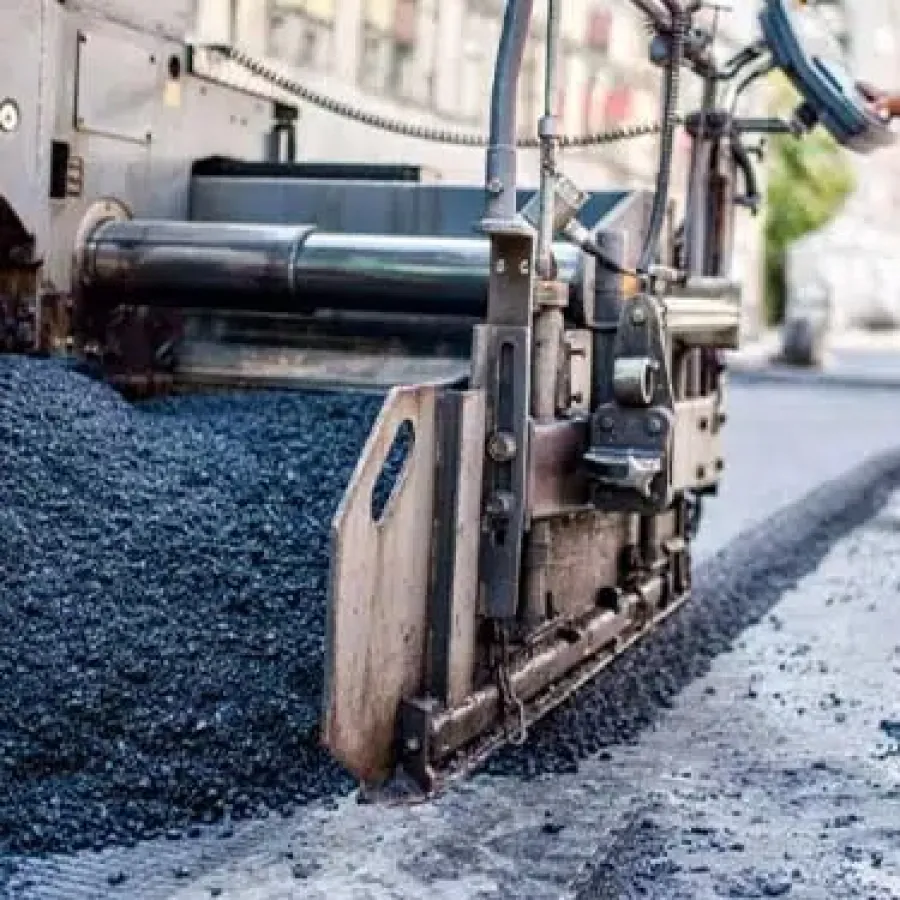 Close-up of asphalt paving machine laying fresh black asphalt on urban road under construction.