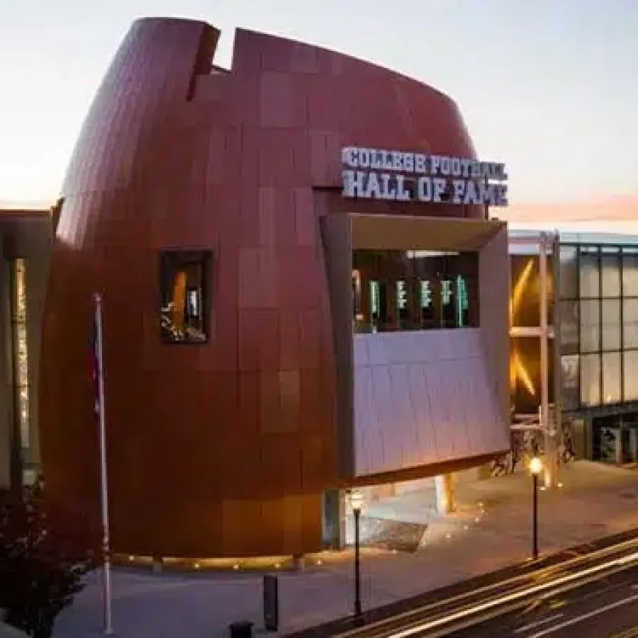 Exterior view of the College Football Hall of Fame building at dusk with glowing lights and street traffic.