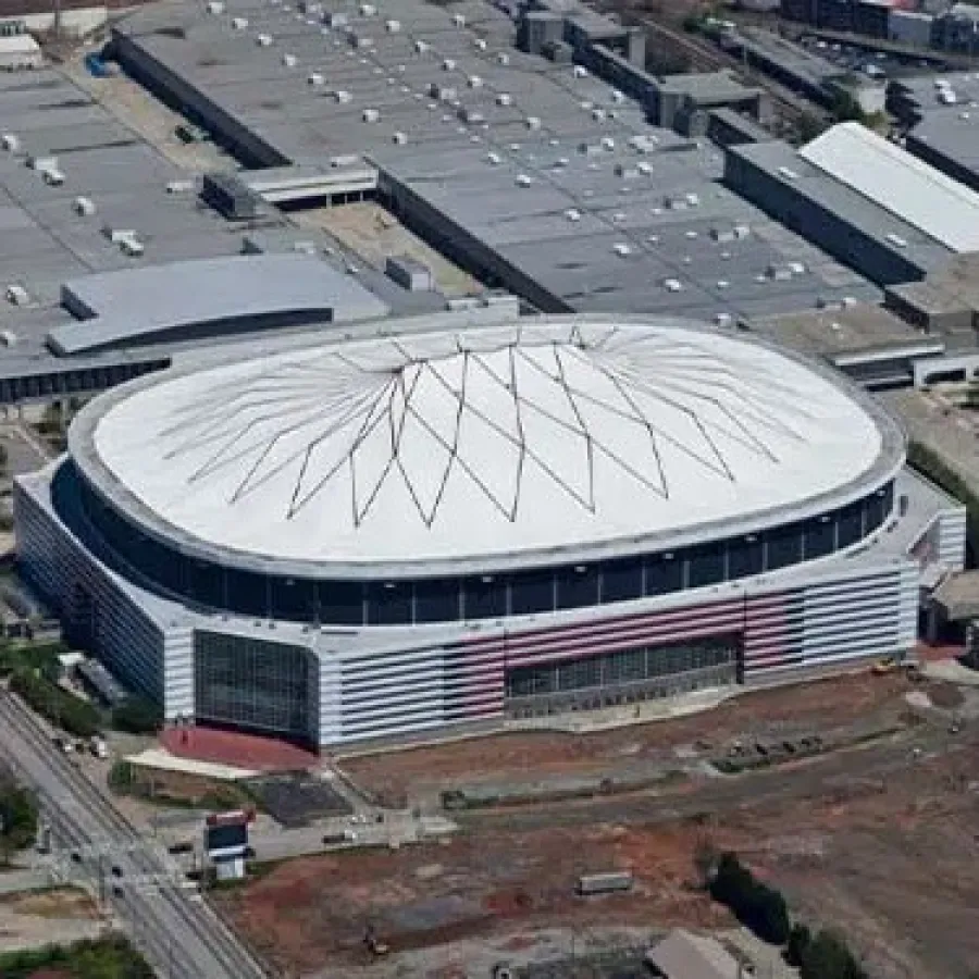 Aerial view of a modern sports arena with a white geometric dome roof surrounded by industrial buildings.