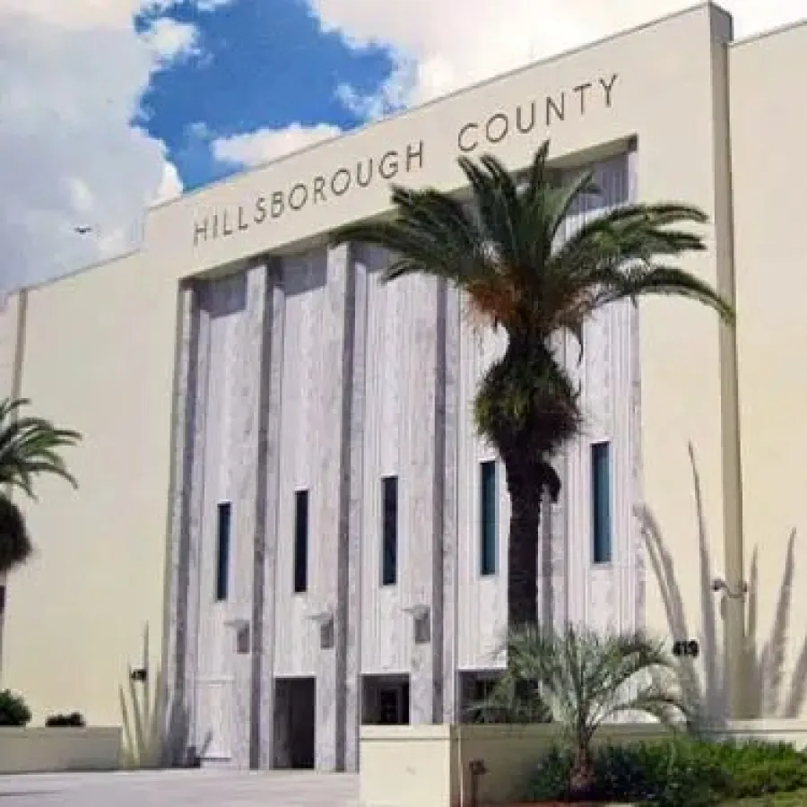 Hillsborough County government building with palm trees and a historic monument under a blue sky.