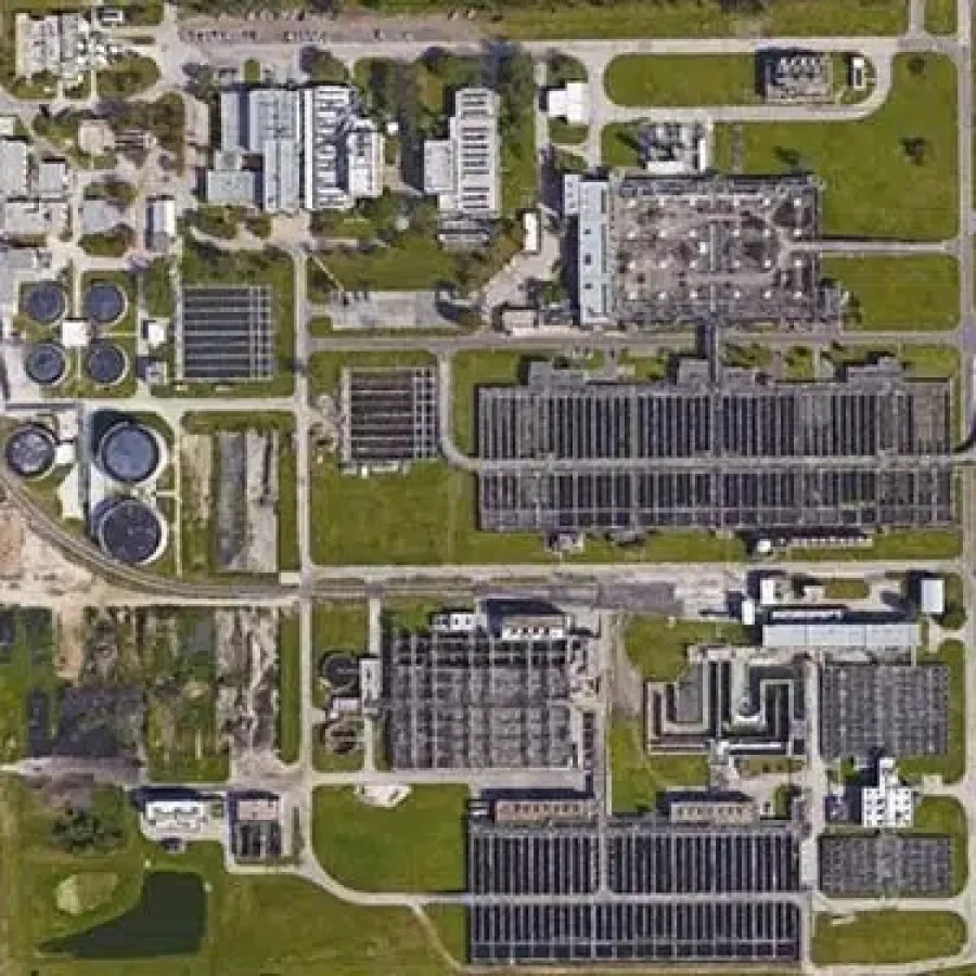 Aerial view of a large wastewater treatment plant with various tanks, buildings, and green spaces.