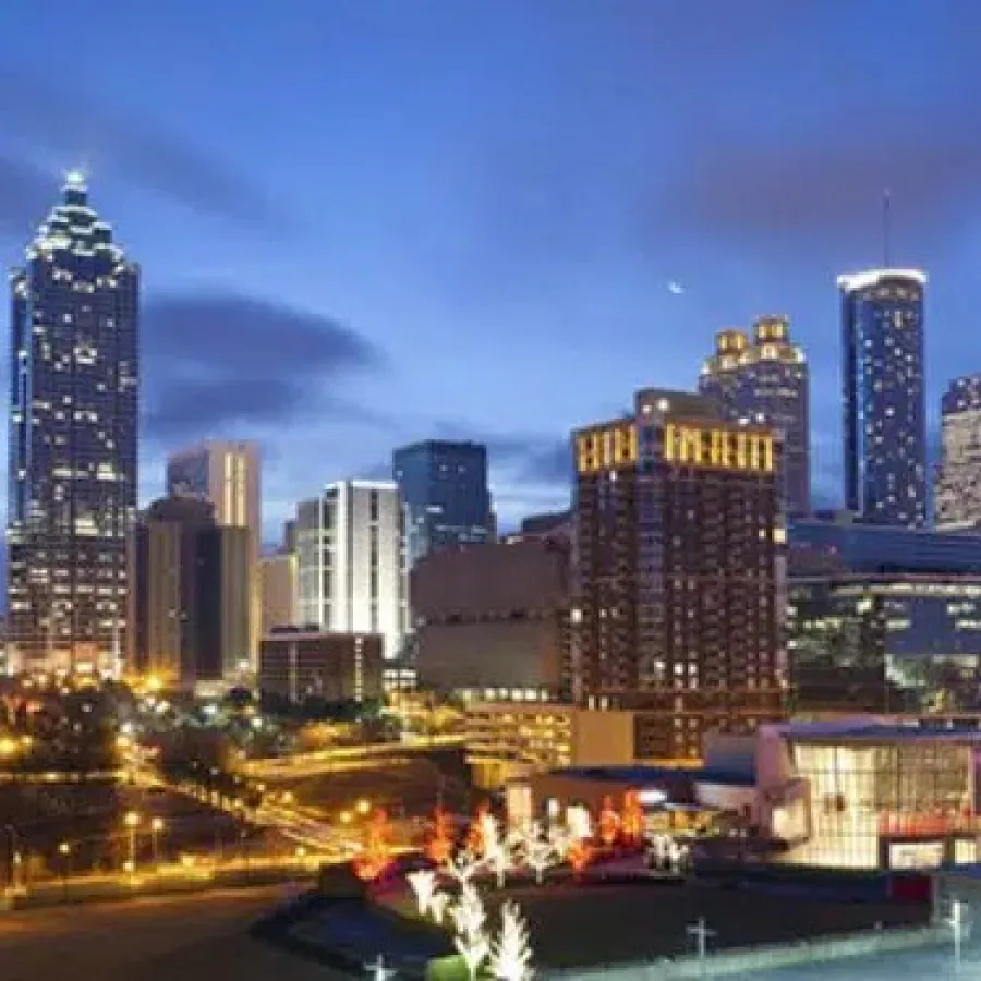 Nighttime cityscape of downtown Atlanta with illuminated skyscrapers and vibrant streetlights under a dark blue sky