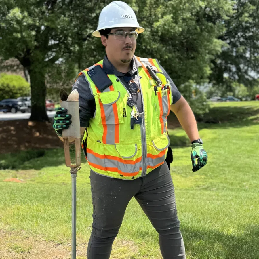Construction worker in safety gear operating equipment on a grassy outdoor site with trees in background