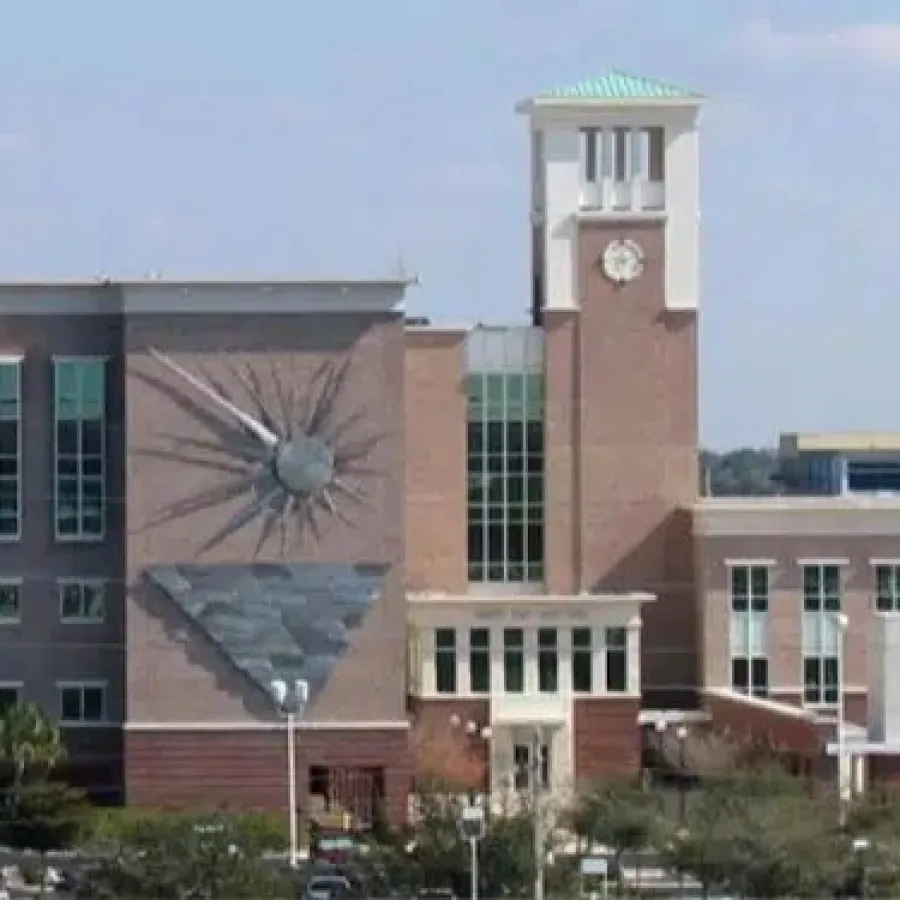 Large brick building with a clock tower and large sundial on a sunny day with blue sky.
