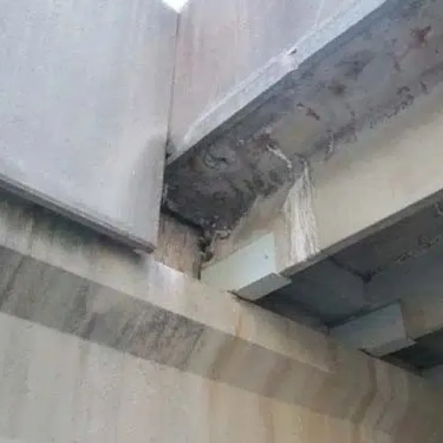 Close-up of concrete and steel bridge structure showing corrosion and water damage.
