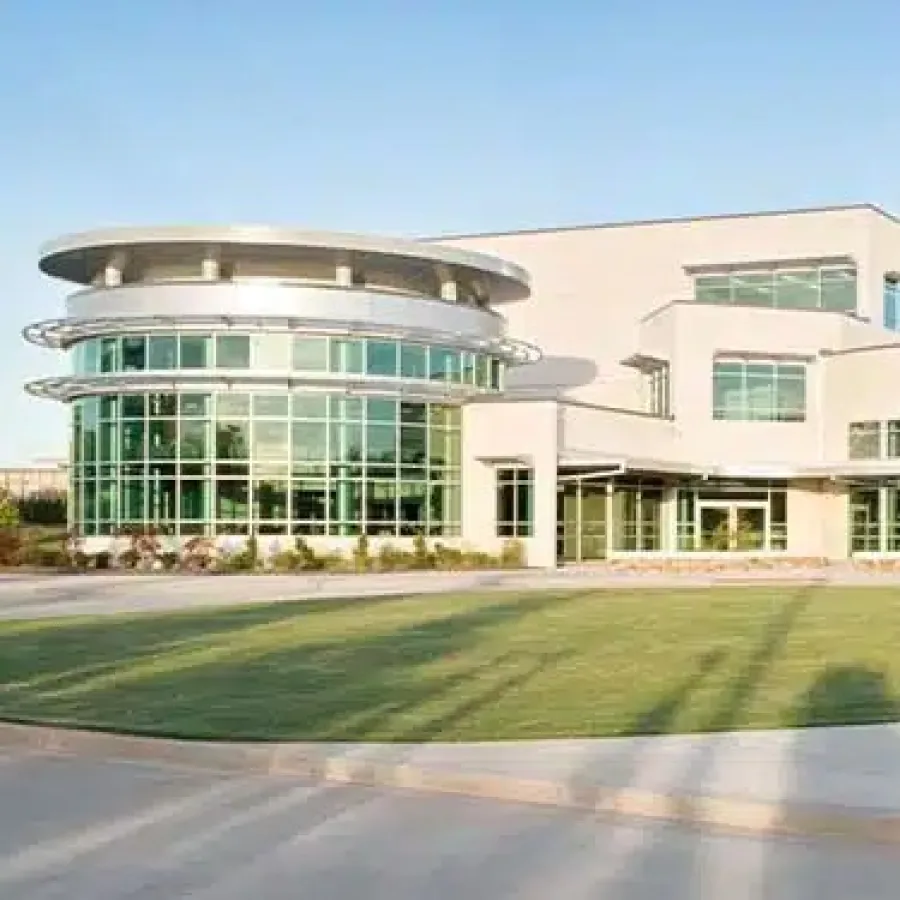 Modern commercial building with large glass windows and a circular green lawn in front under a clear sky