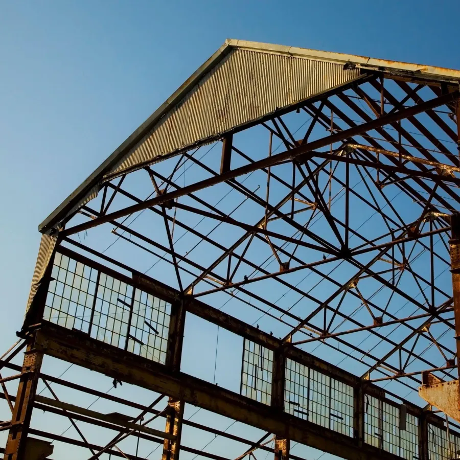 Rusty steel framework of an abandoned industrial warehouse with broken glass panels under clear blue sky